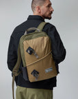 Man wearing a clay and green backpack with a visible Fjällräven logo on a plain background