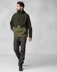 man wearing deep forest-laurel green raincoat jacket with Fjällräven logo and grey trekking trousers