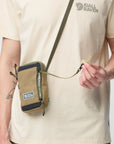 Person wearing a beige t-shirt with Fjäll Räven logo, holding a matching crossbody bag.
