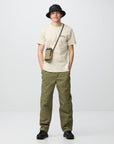 Person wearing a beige t-shirt, green pants, black shoes, and a black hat on a white background