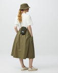 Person wearing a green skirt, white shirt, and hat, holding a black bag on a white background