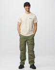 Man wearing a beige t-shirt and green pants on a white background