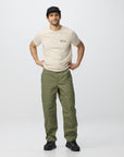 Man wearing a beige t-shirt and green pants on a white background
