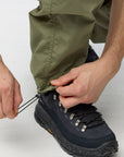 Person tying a black hiking boot with green pants on a white background