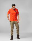 man in orange round neck t-shirt with arctic fox logo and brown trousers