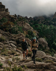 Two hikers on a rocky mountain trail with a cloudy sky.