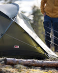 Person standing near a tent with a visible Fjällräven logo in an outdoor setting
