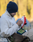 Man sitting outdoors in a natural setting, organizing items in a bag.