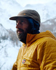 Man wearing a yellow jacket and beige cap outdoors with mountains in the background