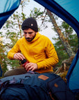 man in mustard yellow fleece jacket with hood drinking water in a tent