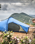 Person setting up a blue tent in a mountainous area with a scenic view.