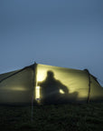 Person walking towards a illuminated tent on a grassy hill at night.
