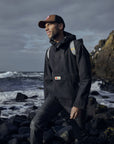man wearing raincoat jacket with Fjällräven logo carrying a backpack and brown cap