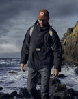 man wearing black raincoat jacket with Fjällräven logo and wearing a brown cap
