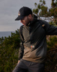 man wearing deep forest-laurel green raincoat jacket with Fjällräven logoand a black cap walking along the forest
