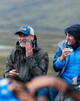 Two men in outdoor clothing sitting together with a scenic background