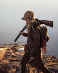 woman in brown jacket carrying a rifle on a rocky mountain