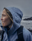 woman in dawn blue windbreaker jacket with hood along rocky coast