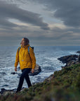 woman wearing yellow waterproof rain jacket with Fjällräven logo walking on the coast
