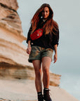 woman wearing black top and beige bermudas shorts carrying a red sling bag