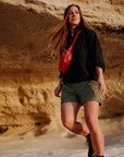 woman wearing black top and green bermudas shorts carrying a red sling bag