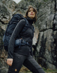 woman in a black top and black bottom carrying a trekking backpack