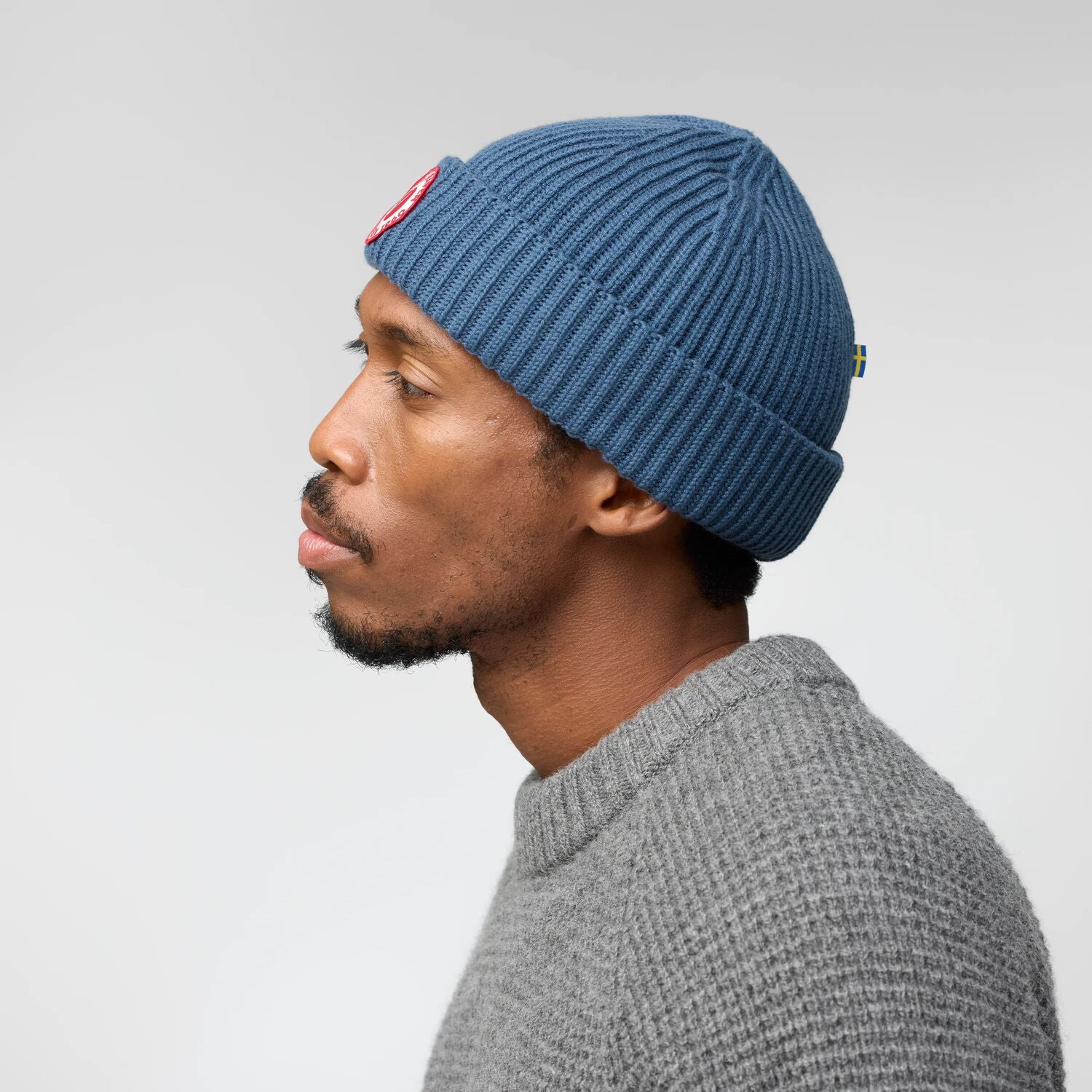 Man wearing a blue knit beanie and gray sweater against a plain background