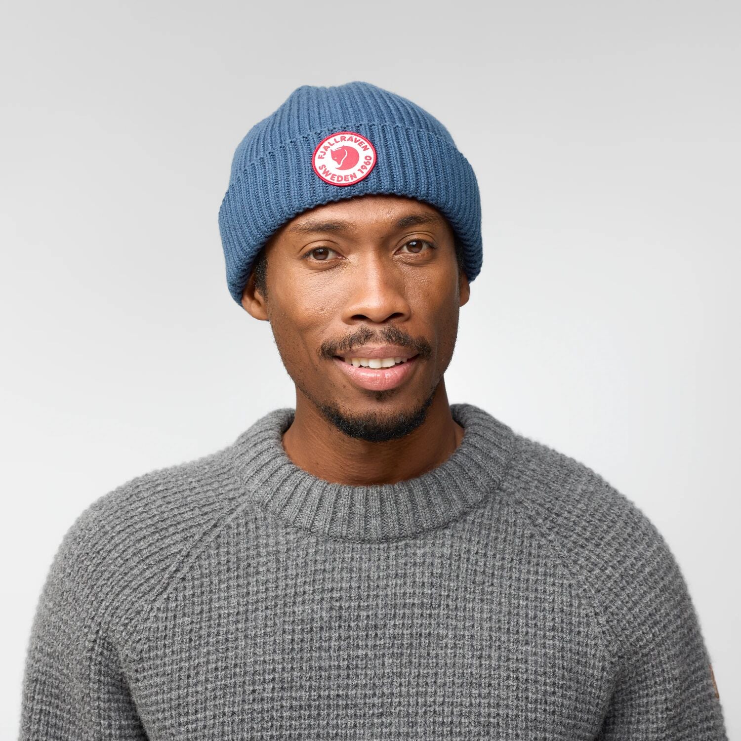 Man wearing a blue beanie with a Fjällräven logo on a plain background