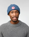 Man wearing a blue beanie with a Fjällräven logo on a plain background