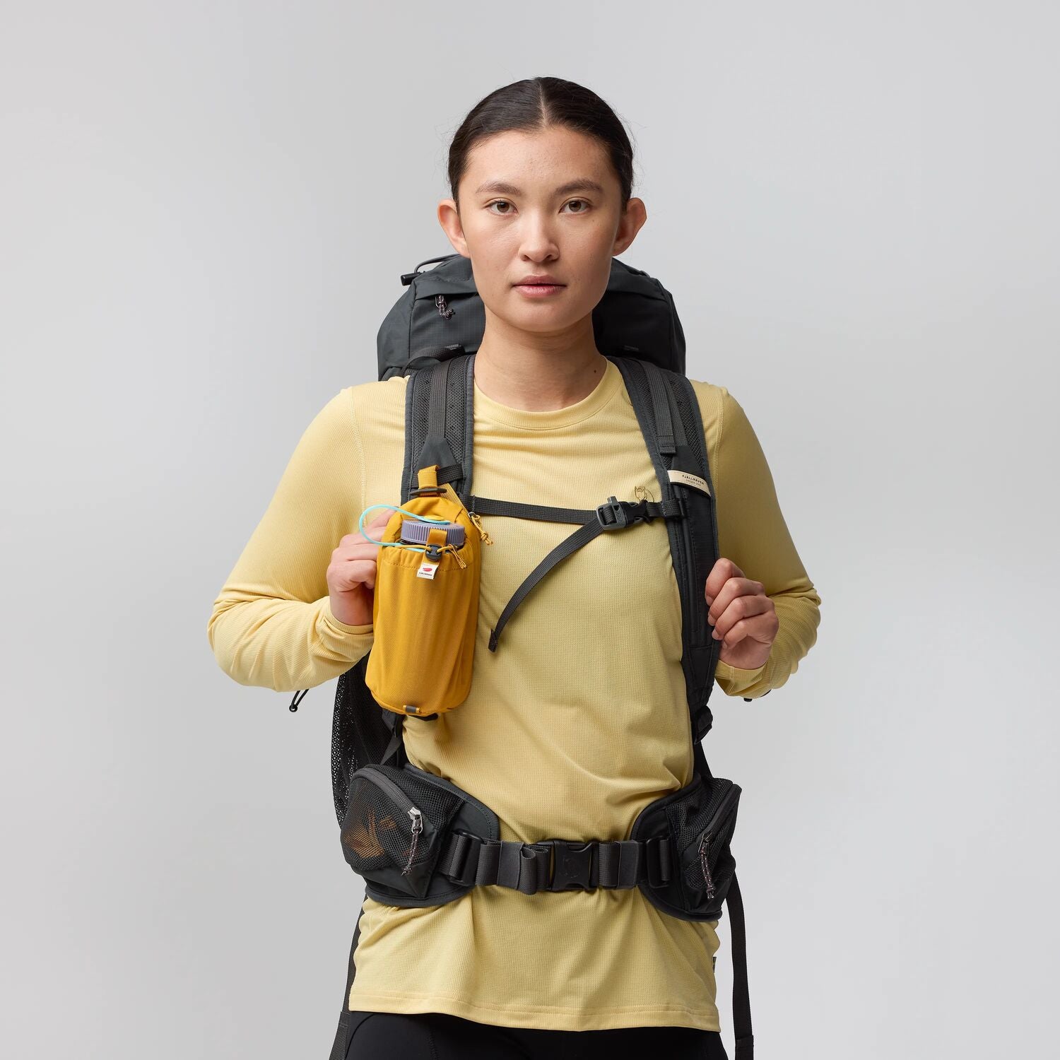 Person wearing a black backpack and yellow shirt on a gray background