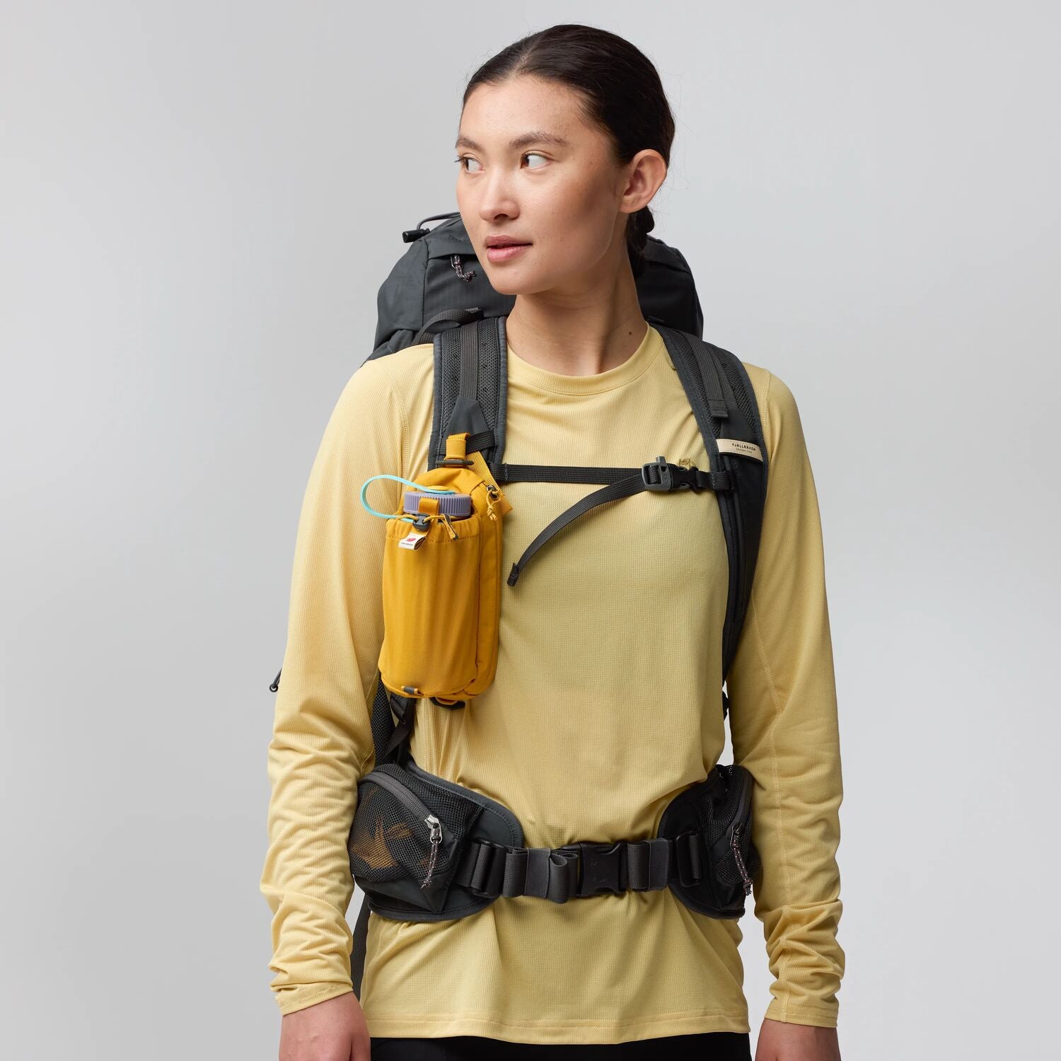 Person wearing a yellow long-sleeve shirt with a black backpack and yellow hydration pack on a gray background