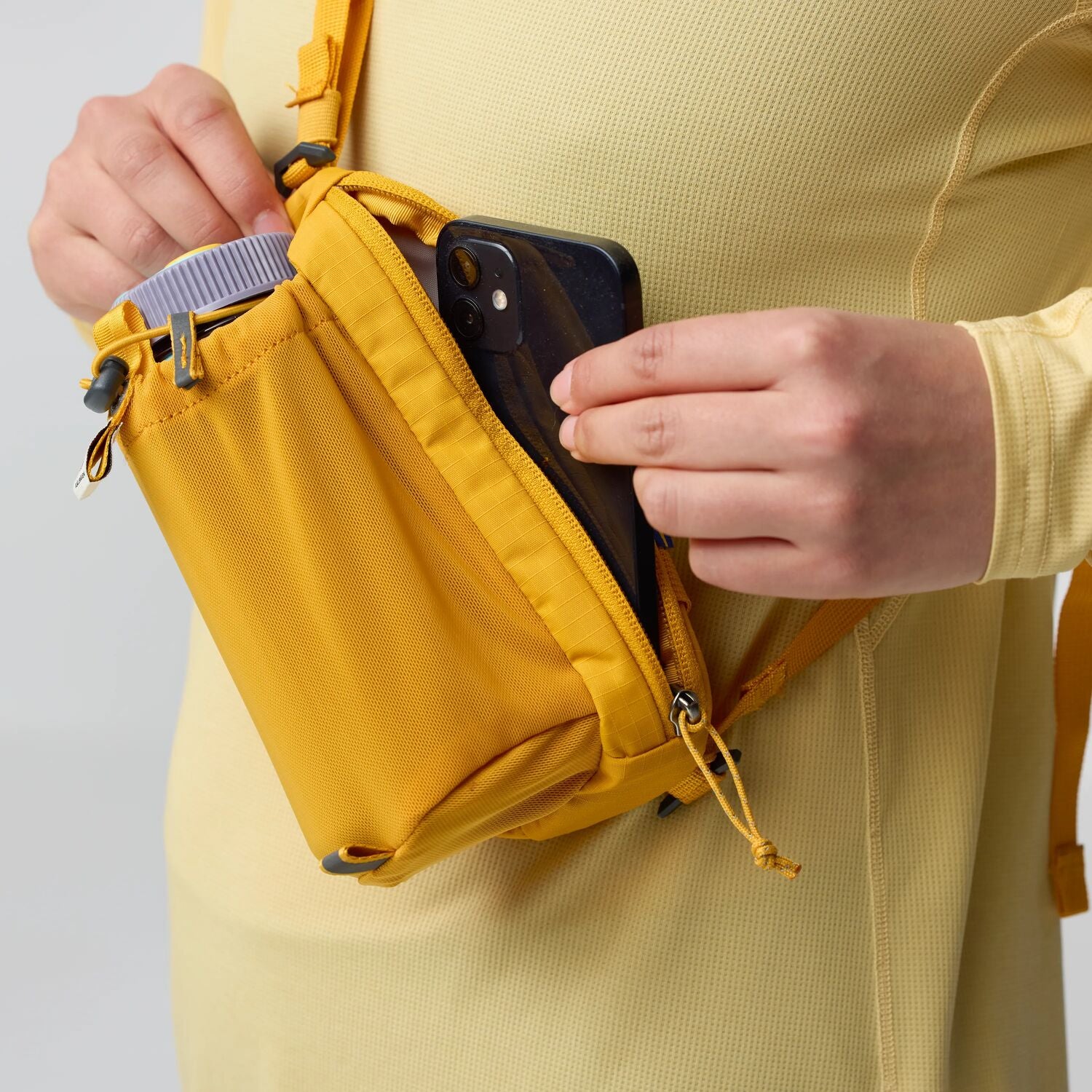 Person holding a yellow waist bag with a phone inside, wearing a yellow shirt.