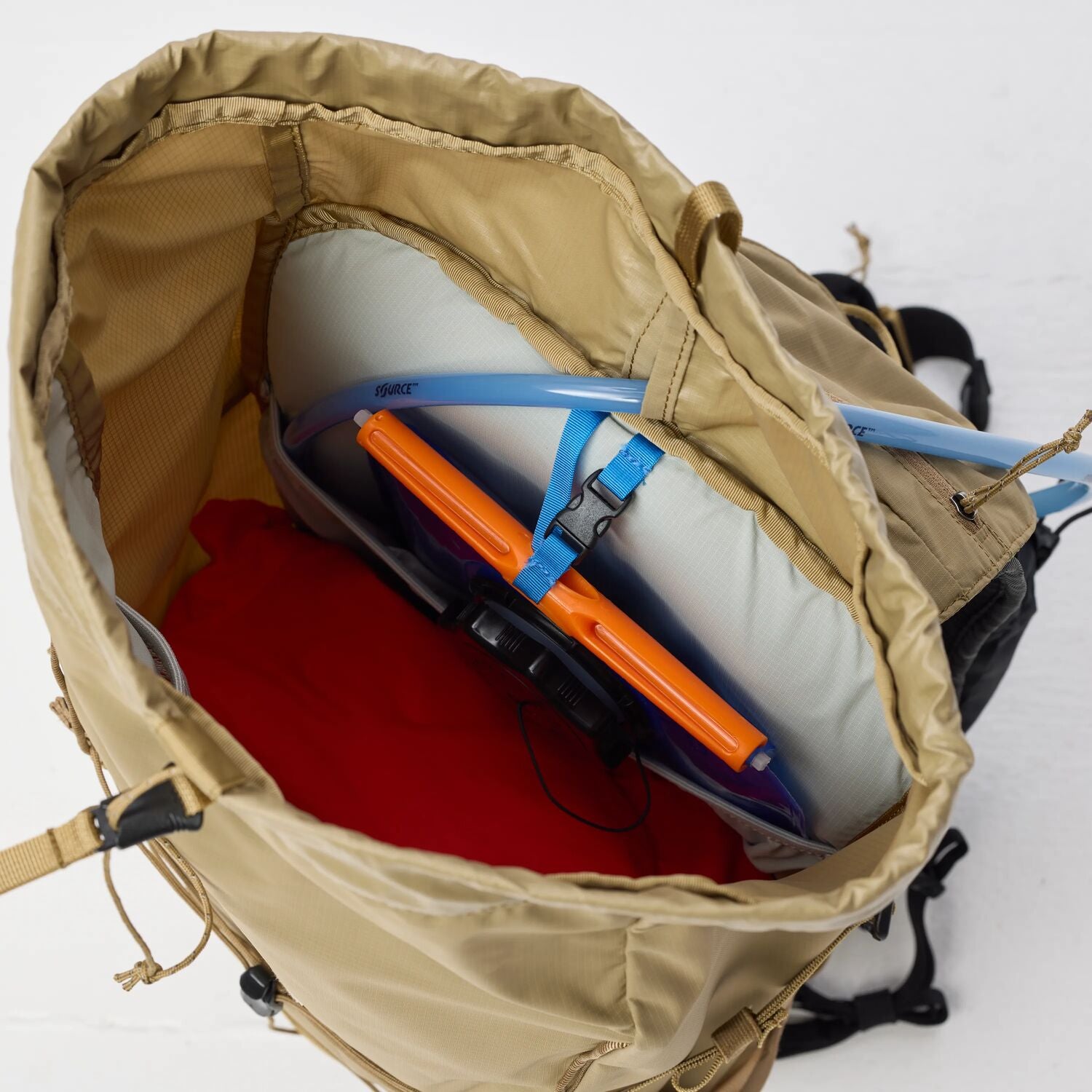 Open beige backpack with camping gear including a sleeping pad and hydration bladder on a white background
