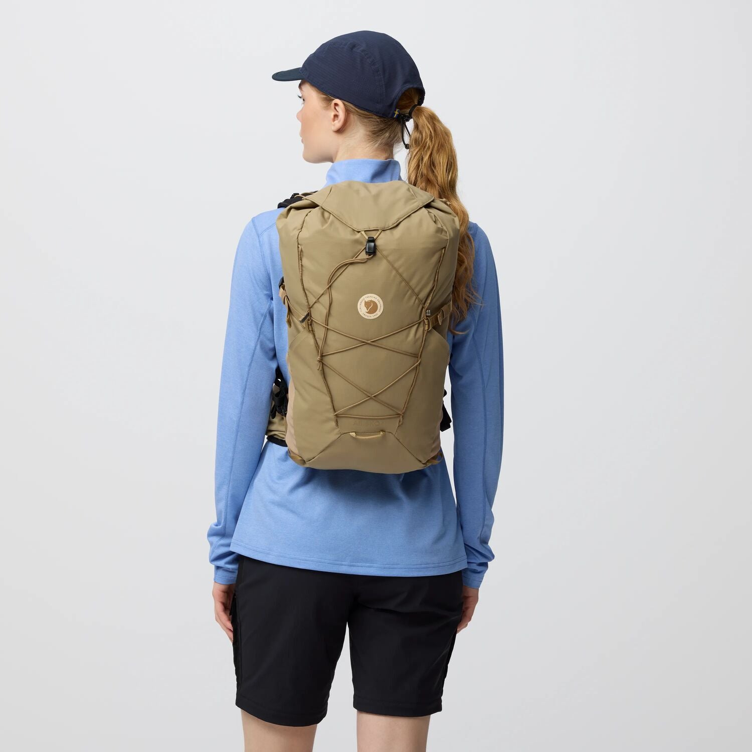 Person wearing a beige backpack with a Fjällräven on a plain background