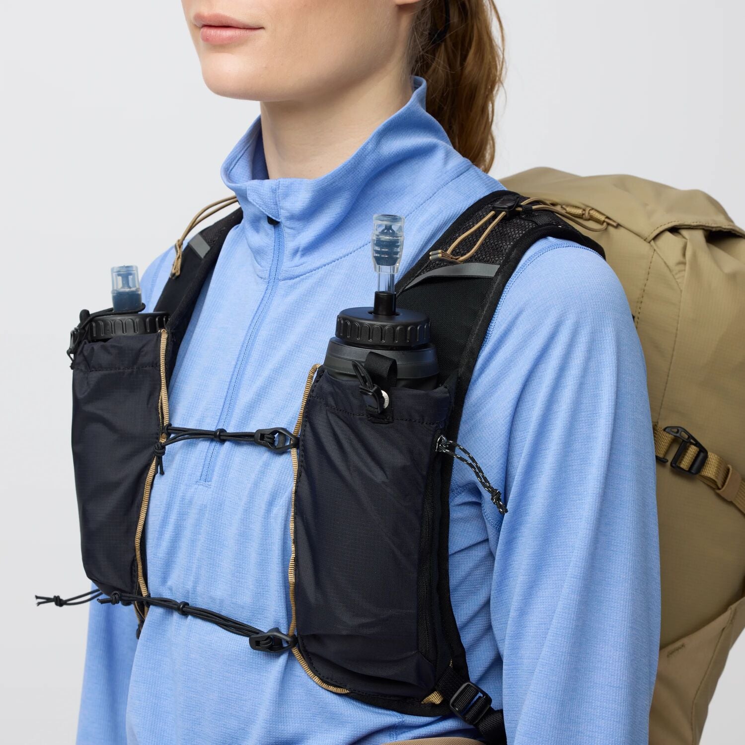 Person wearing a black hydration vest with water bottles on a plain background