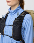 Person wearing a black hydration vest with water bottles on a plain background