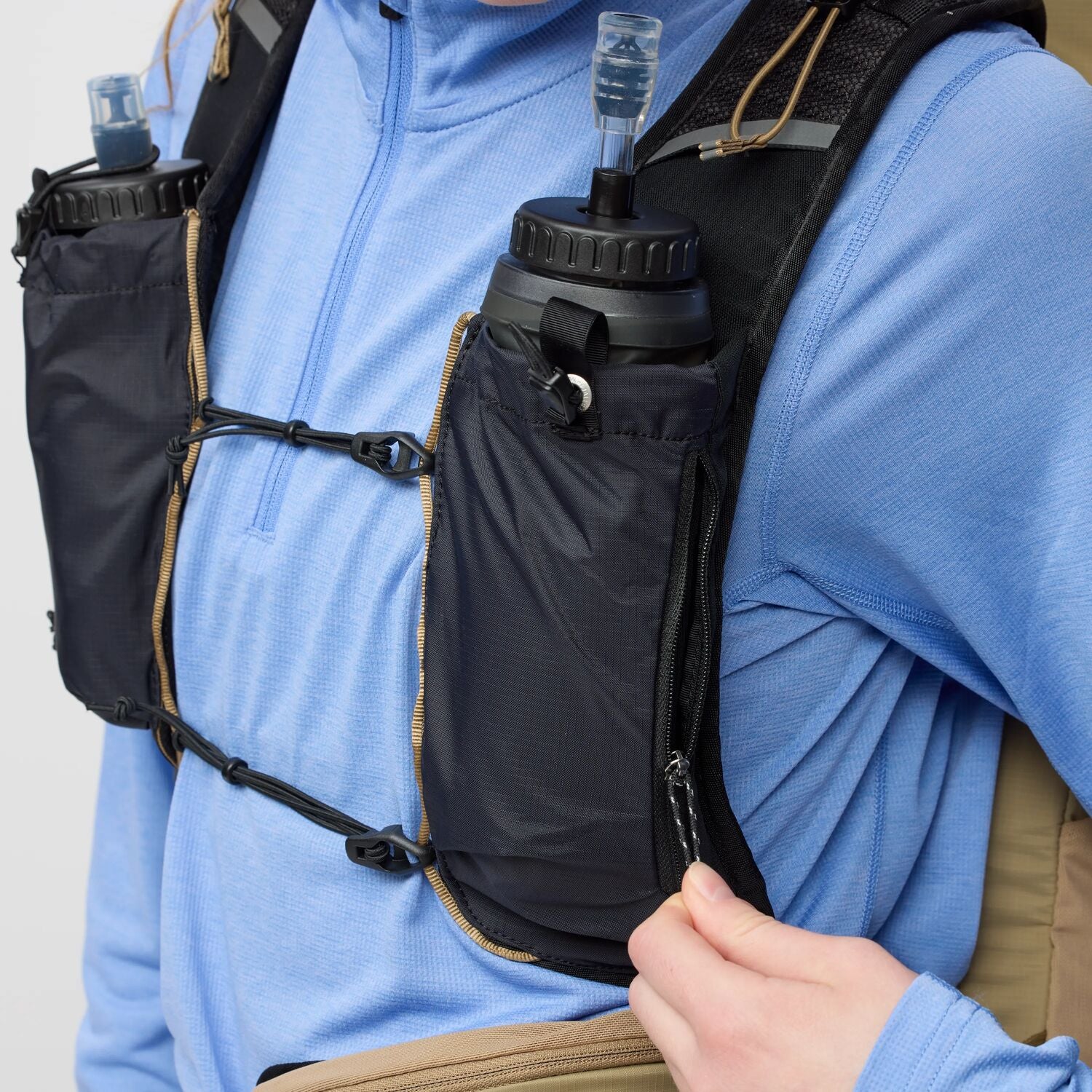 Person wearing a blue jacket with a black hydration pack on a plain background