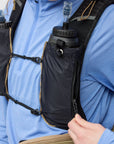 Person wearing a blue jacket with a black hydration pack on a plain background