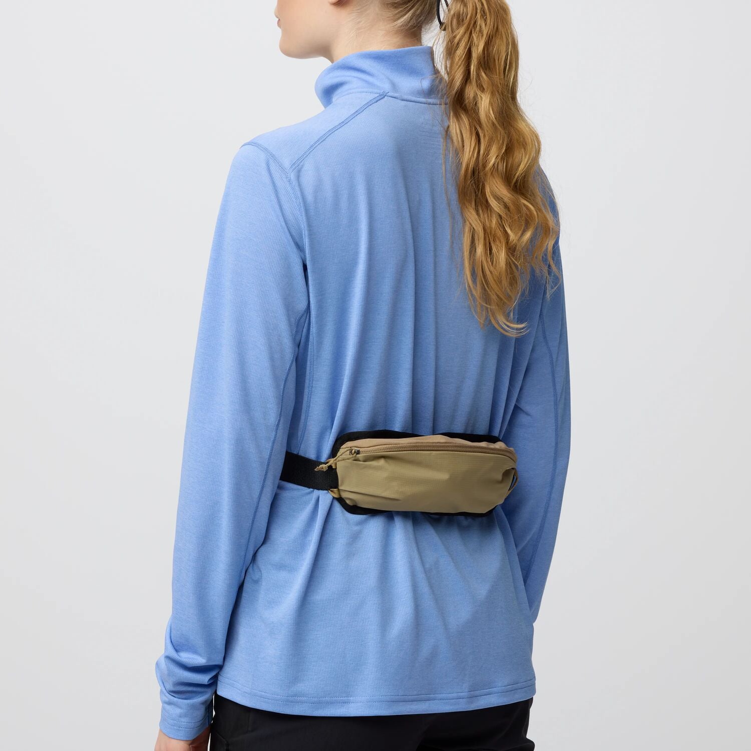 Person wearing a blue long-sleeve shirt with a beige waist bag pouch on a light gray background