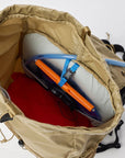 Open beige backpack with camping gear including a hydration bladder on a white background
