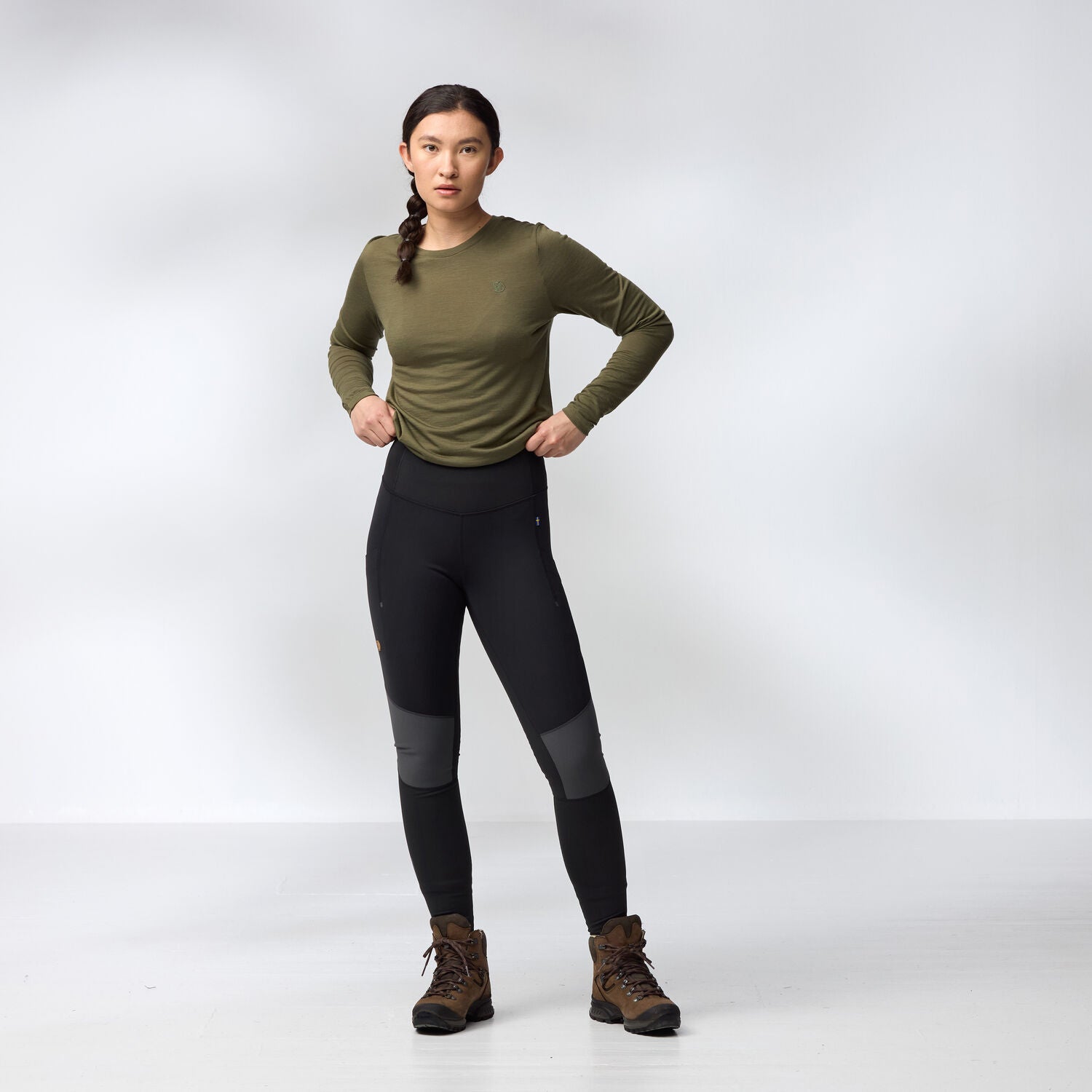 Woman wearing a green long-sleeve top and black leggings tights on a white background