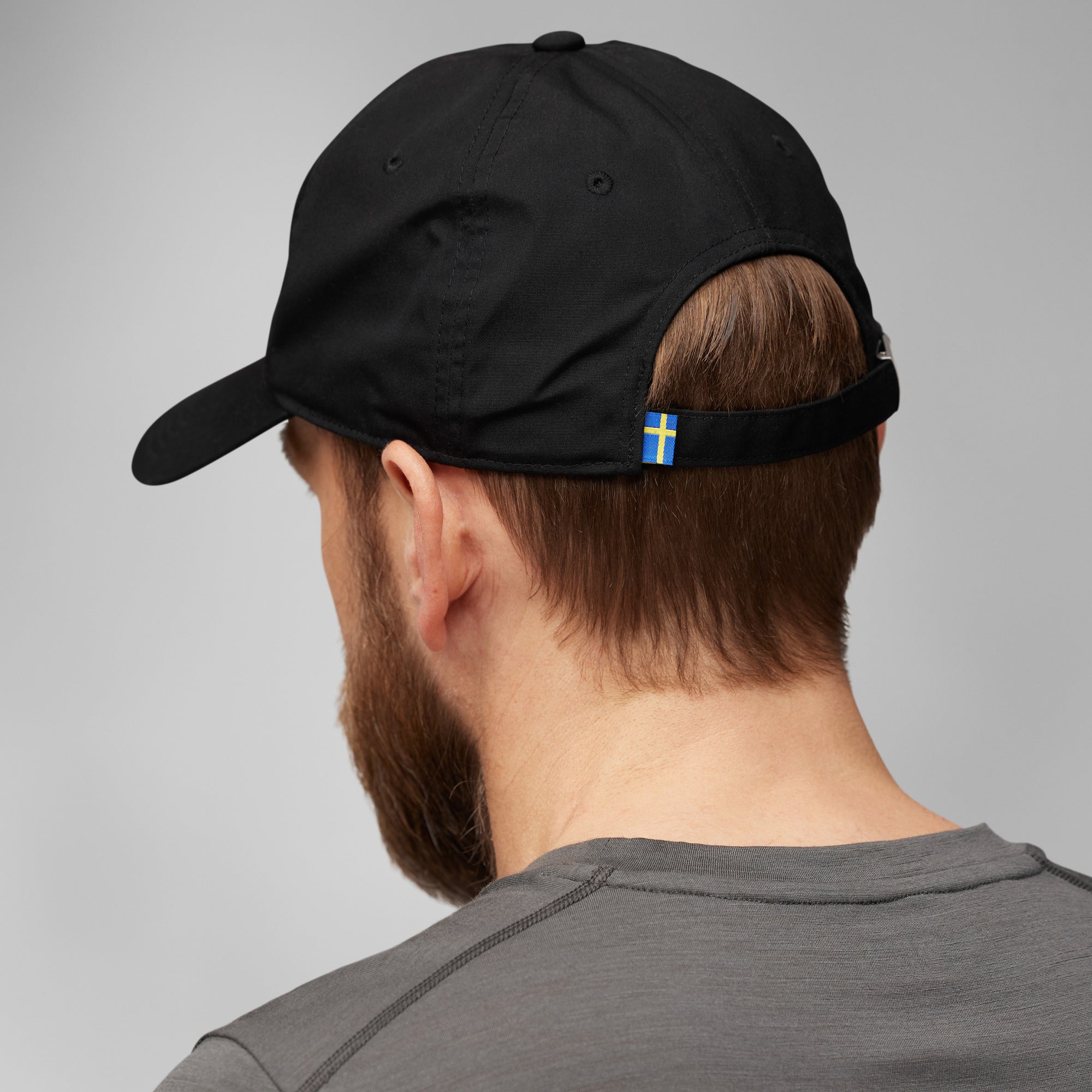 Person wearing a black cap with a small sweden flag emblem on a gray background