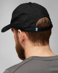 Person wearing a black cap with a small sweden flag emblem on a gray background
