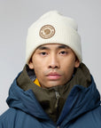 Person wearing a white beanie with a Fjällräven logo and a blue jacket on a gray background