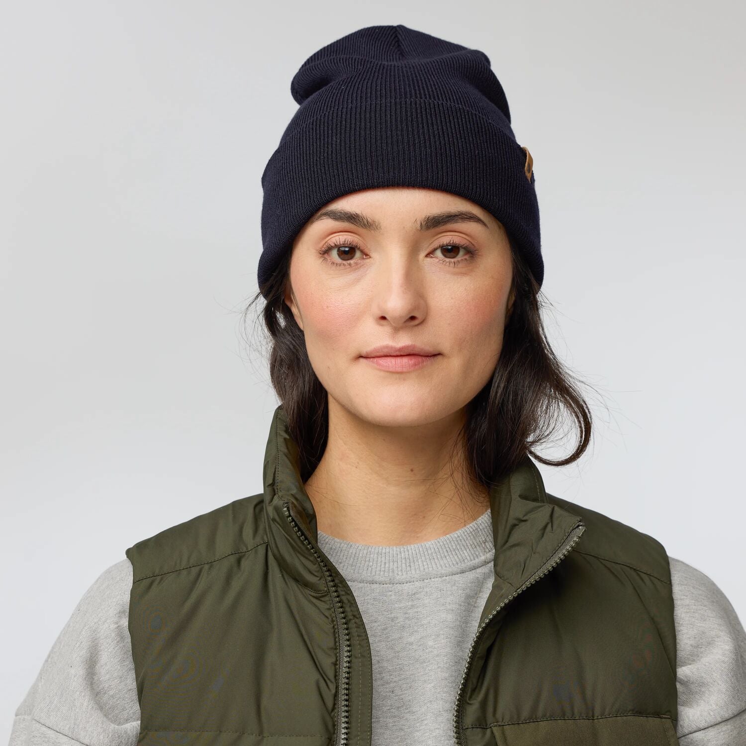 Person wearing a navy beanie and green vest on a light gray background
