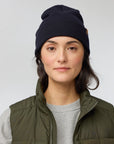 Person wearing a navy beanie and green vest on a light gray background