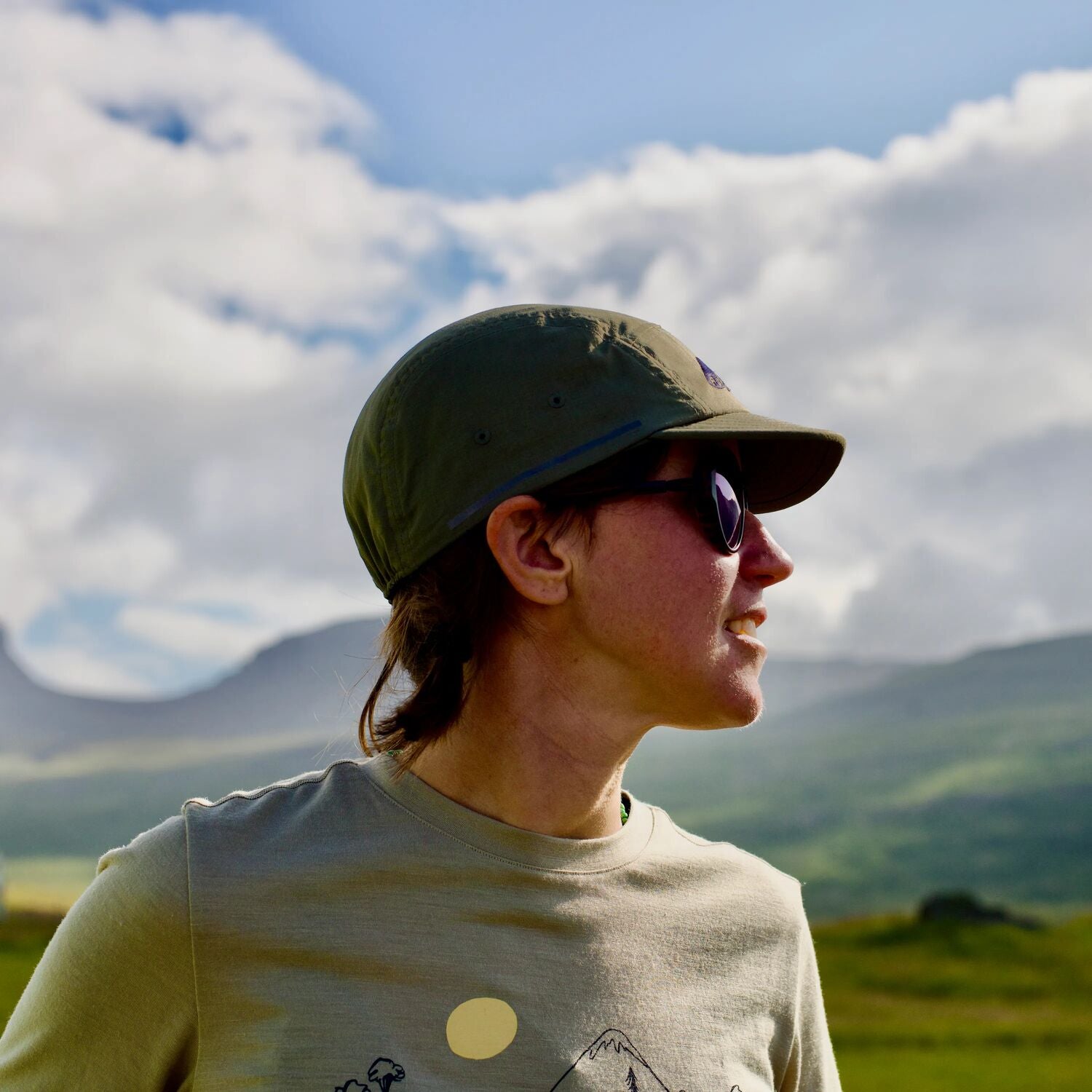 Person wearing a cap and sunglasses with mountains in the background