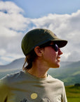 Person wearing a cap and sunglasses with mountains in the background