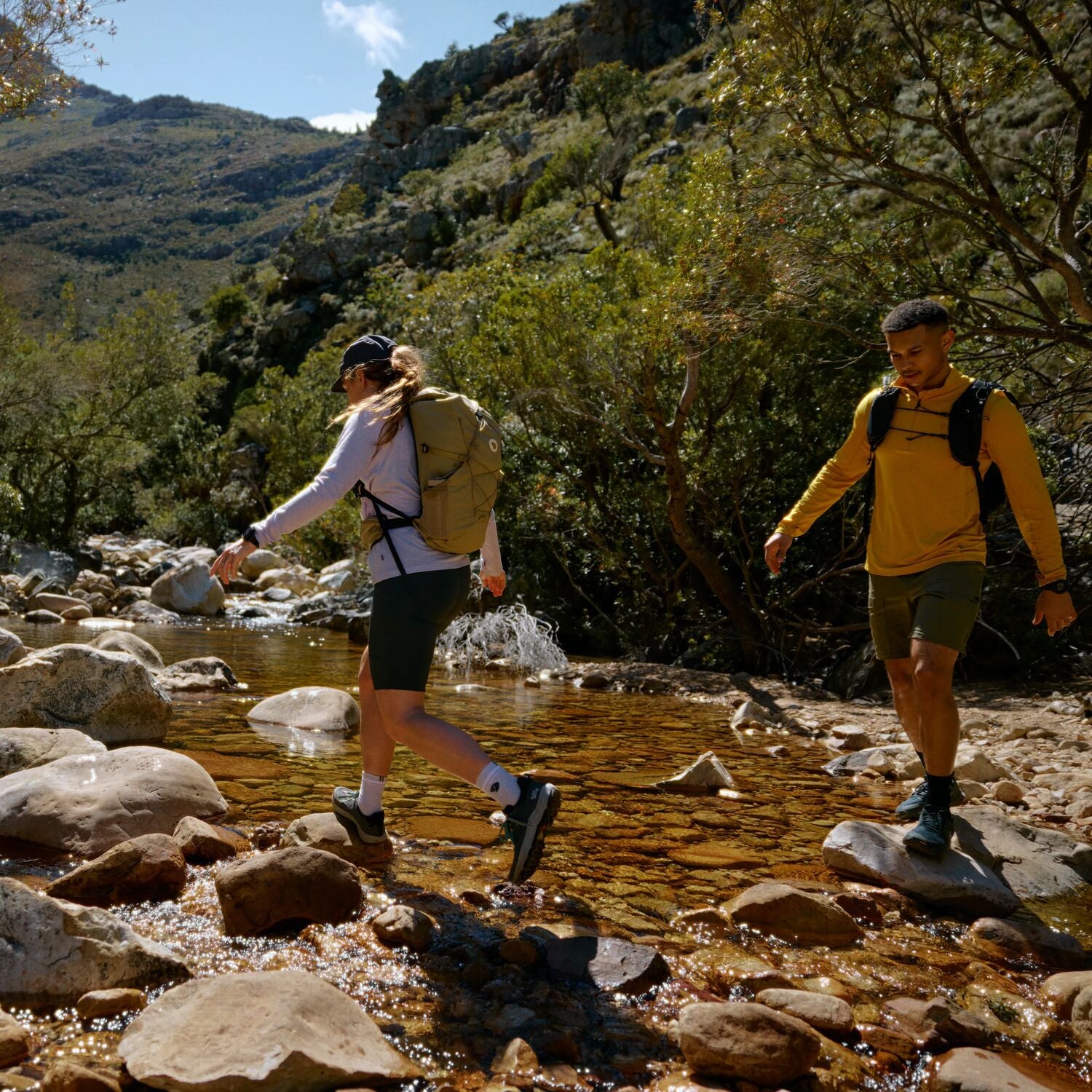 Two hikers crossing a stream in a mountainous area