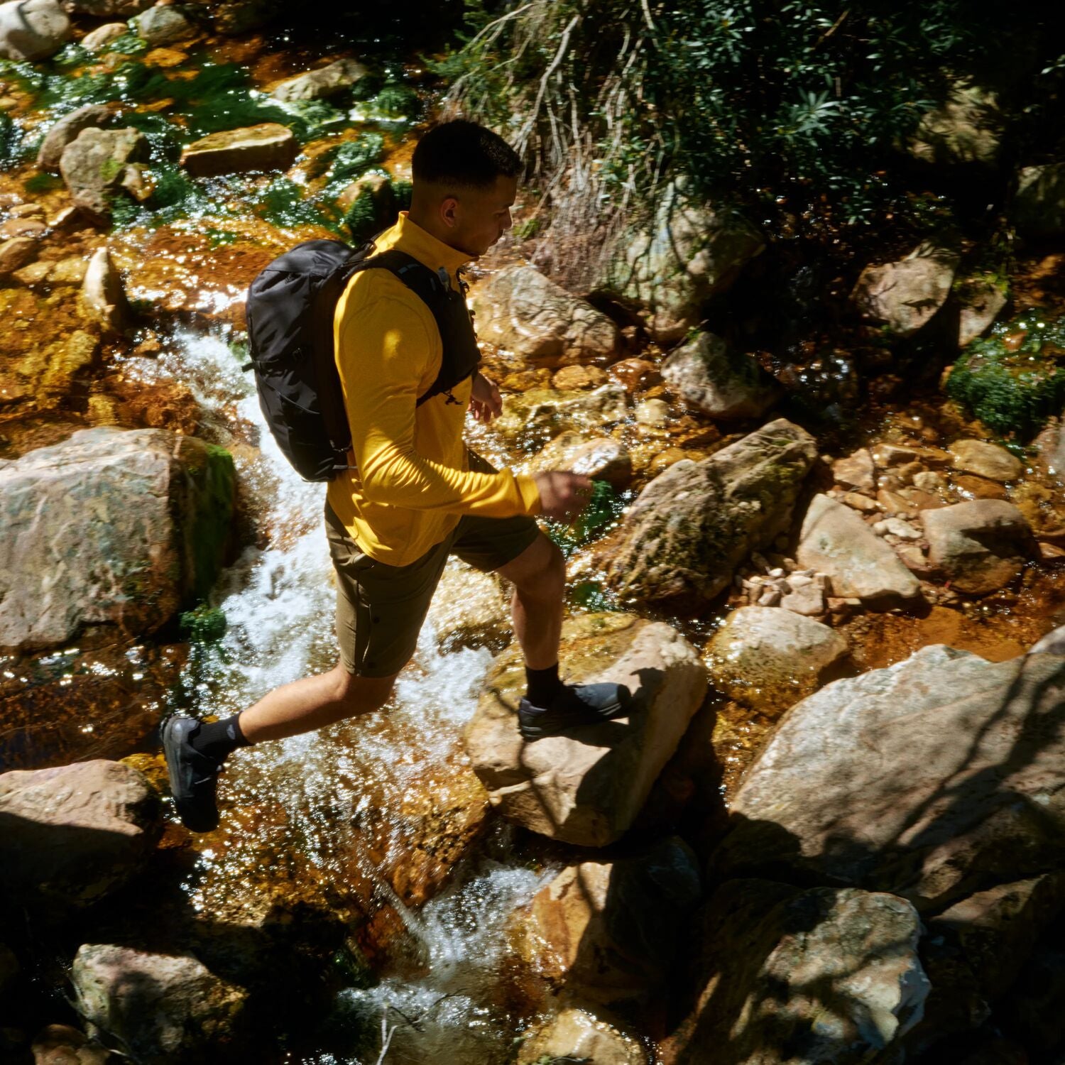 Person hiking through a rocky stream wearing a yellow shirt and black backpack.